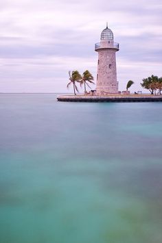 an island with a light house in the middle and palm trees on it's side