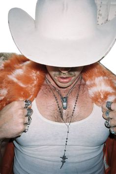 a man wearing a white cowboy hat and holding his hands on his chest with an orange fur stole around his shoulders