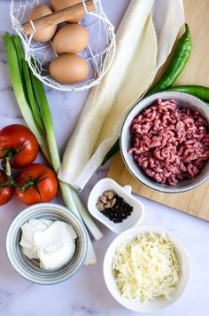 ingredients to make an italian dish laid out on a marble counter top, including tomatoes, green beans and eggs