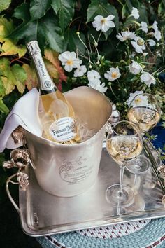 two wine glasses and a champagne bottle in an ice bucket on a tray with flowers