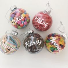 four glass ornaments with candy in them on a white surface, one has the word peace and three are filled with candies