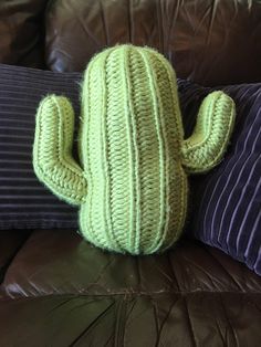 a green knitted cactus sitting on top of a brown leather couch next to pillows