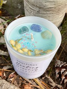 a cup filled with blue liquid sitting on the ground next to pine cones and leaves