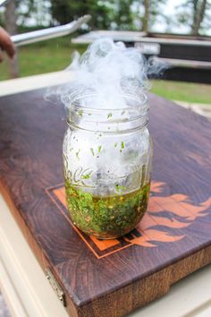 a jar filled with green stuff sitting on top of a wooden table next to a person