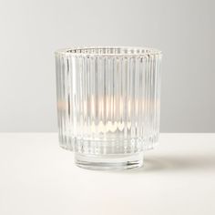 a clear glass candle holder sitting on top of a white table next to a wall