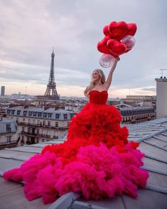 a woman in a red and pink dress on top of a roof holding balloons with the eiffel tower in the background