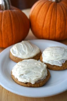 three cookies with frosting on a plate next to pumpkins