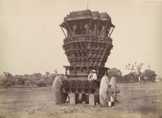 two men standing in front of an elaborately designed cart, possibly from the 19th century