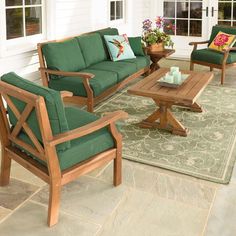 an outdoor living room with green furniture and flowers on the patio table, chairs, and rug