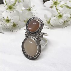 Not only does this ring have a dreamy peach moonstone but it also has an amazing cream moonstone too.  The coloring draws you.  Once you’re there, the pearlescent glow will keep you there.  The peach moonstone is a soft but rich terracotta color.  Equally important is the creamy coloring of the ivory moonstone.  Both stones sit nestled within silver bezel cups.  The peach stone is accented with a hammered silver braid.  A simple wire frame wraps around the ivory stone. Moonstone Rings With Natural Stones, Adjustable Elegant Moonstone Ring Oval Cabochon, Large Stone Moonstone Ring, Moonstone Oval Cabochon Ring, Untreated Round Moonstone Ring, Bohemian Moonstone Cabochon Ring, Moonstone Ring With Large Stone, Bohemian Round Cabochon Moonstone Ring, Bohemian Cabochon Moonstone Ring