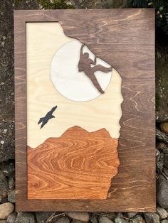 a wooden plaque with a silhouette of a person on top of a mountain and a bird flying in the sky