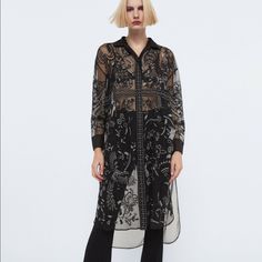 Semi-Sheer Collared Blouse. Long Cuffed Sleeves. Contrast Embroidered Detailing. Asymmetric Hem With Side Vents. Button-Up Front. Embroidered Long Sleeve Blouse For Evening, Long Sleeve Embroidered Blouse For Evening, Embroidered Long Sleeve Blouse For Night Out, Evening Floral Embroidered Long Sleeve Blouse, Elegant Embroidered Button-up Blouse, Chic Evening Blouse With Floral Embroidery, Black Button-up Blouse With Floral Embroidery, Black Floral Embroidery Button-up Blouse, Chic Embroidered Daywear Blouse