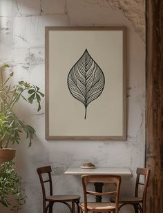 a painting hanging on the wall above a table with two chairs and a potted plant