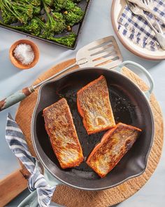 three pieces of fish cooking in a frying pan with broccoli on the side