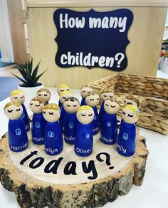 a group of blue wooden dolls sitting on top of a tree stump in front of a sign that says how many children?