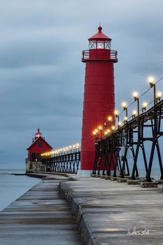 a red light house sitting on top of a pier next to the ocean at night