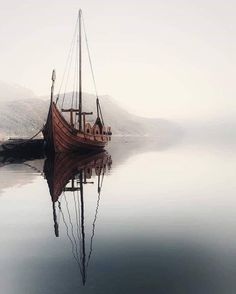 an old boat is sitting in the water on a foggy day with mountains in the background