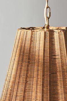 a wicker lamp shade hanging from a metal hook on a gray background with an orange light bulb in the center