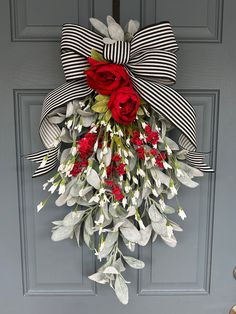 a wreath with red roses and white flowers hanging from the front door, on a gray door