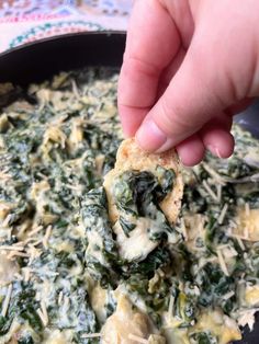 someone is dipping something into a skillet with spinach and cheese on it,