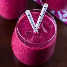 two glasses filled with purple smoothie on top of a wooden table