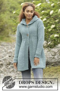 a woman wearing a blue coat and jeans standing in front of some rocks with her hands on her hips