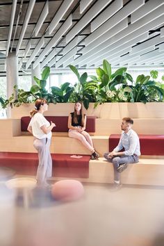 three people are sitting on benches in an office building with plants and potted plants