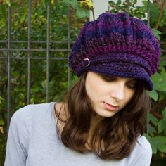 a woman wearing a knitted hat with buttons on the front and side, standing in front of a fence