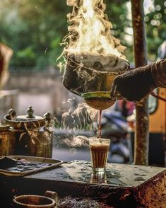 a person pouring liquid into a glass on top of a table with pots and pans