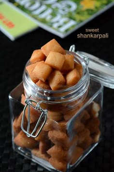 a glass jar filled with small pieces of food on top of a black table next to a book