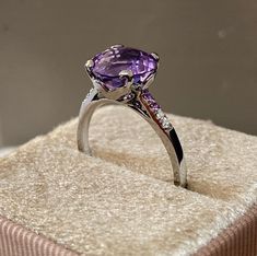 A sparkling solitaire with an amethyst gem held into a corolla of 18kt gold, flanked with brillant-cut diamonds accents on a cathedral style setting. Every detail is delightful in this ring, from the prongs in the shape  of a flower corolla, to the mix of amethyst and diamond as accent stones on the gallery and the delicate facets that reflect the light. The gold has been ionized to a grey finish to enhance the purple hue of the stone. - Size: UK L1/2, US 6, FRANCE 52 - Weight: 2,9 gr - Hallmark Elegant Yellow Gold Amethyst Ring With Brilliant Cut, Luxury Purple Sapphire Ring With Diamond, Luxury Amethyst Ring With Emerald Cut Diamond, Luxury Diamond Cut Amethyst Ring For Formal Events, Luxury Emerald Cut Amethyst Ring With Diamond Setting, Luxury White Gold Amethyst Ring With Diamond, Luxury Platinum Amethyst Ring With Brilliant Cut, Luxury Emerald-cut Diamond Amethyst Ring, Luxury Amethyst Cushion Cut Ring For Formal Occasions