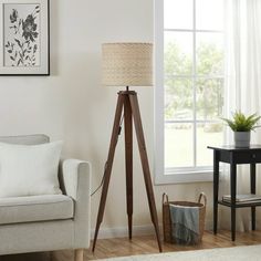 a living room with a white couch and wooden tripod floor lamp in front of a window