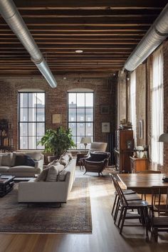 a living room filled with lots of furniture next to tall windows and wooden floors in front of brick walls