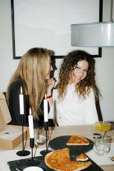 two women sitting at a table with pizza and candles in front of them, smiling