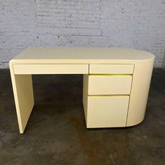 a white desk sitting on top of a floor next to a brick wall and cement floor