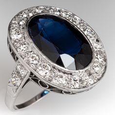 This beautiful ring is centered with one (1) laboratory grown sapphire set into a bezel setting. The sapphire is bordered with sixteen (16), bead set, old European/transitional brilliant/single cut diamonds. The shoulders of the ring are each accented with two (2), bead set, round transitional brilliant cut diamonds. The ring measures 20.2mm at the top, rises 5.3mm above the finger, tapering to 1.2mm wide and 0.6mm thick at the base of the shank. It is currently a size 5.5. Four of the melee diamonds are unnoticeably chipped. Formal Sapphire Ring With 17 Jewels In Platinum, Classic Sapphire Ring Oval Cabochon, Formal Fine Jewelry Sapphire Ring Oval Cabochon, Formal Sapphire Ring With Bezel Setting And Oval Cabochon, Oval Cabochon Sapphire Ring For Formal Events, Classic Oval Cabochon Sapphire Ring With Bezel Setting, Classic Sapphire Ring With Oval Cabochon Bezel Setting, Oval Sapphire Ring In Platinum For Formal Occasions, Platinum Oval Cabochon Ring With Center Stone