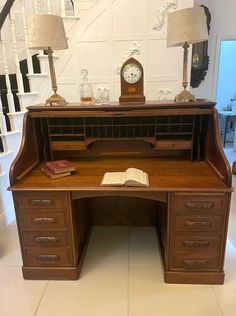 an old fashioned desk with a clock and lamp on the top, next to a staircase