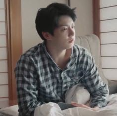 a young man sitting on top of a bed next to a white pillow and pillows