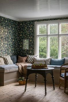 a living room filled with furniture next to a window covered in wallpaper and pillows