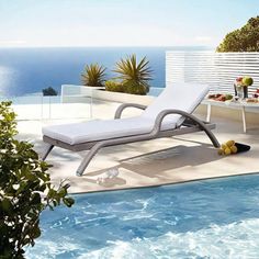 an outdoor lounge chair sitting next to a swimming pool with the ocean in the background