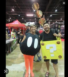 two people dressed up as pacman and mushroom at an indoor convention center with balloons in the air