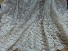 an image of a white lace curtain with flowers on the bottom and side, laying on top of a table