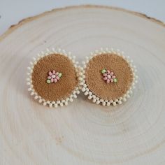 two small white and pink flowers are placed on top of a wood slice with beads