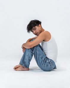 a young man sitting on the ground with his arms crossed and looking at the camera