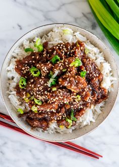 a bowl filled with meat and rice next to chopsticks on a marble surface