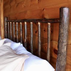 a wooden bed frame with white pillows in a cabin style bedroom, next to a wall made of wood planks