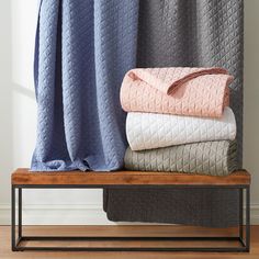 three blankets stacked on top of each other in front of a window with blue and pink curtains