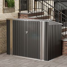 a metal storage shed sitting on the side of a brick building next to a stair case