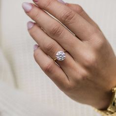 a woman's hand with a diamond ring on her left hand, wearing a white sweater and gold bracelet