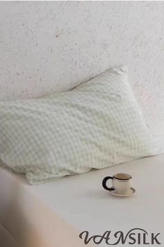 a white pillow sitting on top of a bed next to a cup